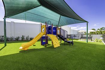 A playground with a yellow slide and a blue slide under a green canopy.